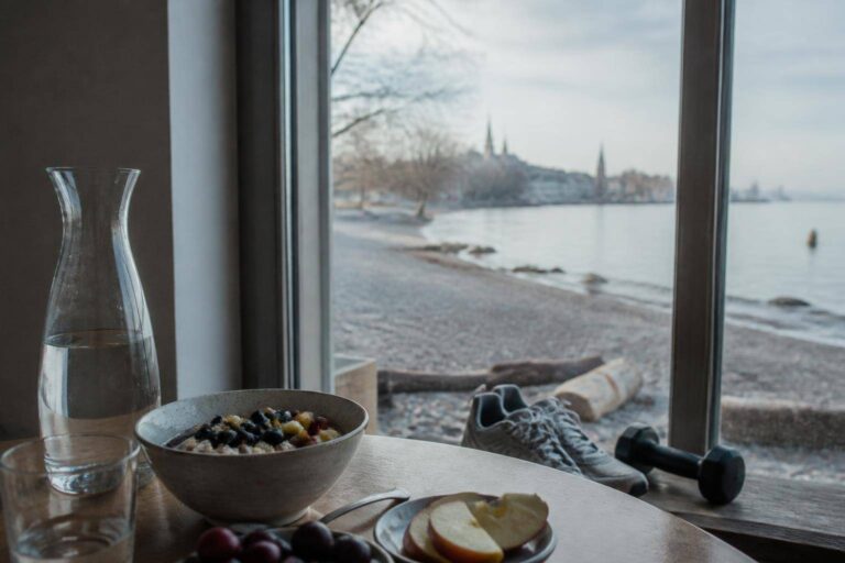 Frühstückstisch mit Haferflocken, Obst und Wasserkaraffe, Blick aufs Konstanzer Seeufer – Abnehmen nach den Feiertagen