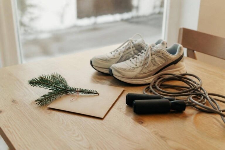 Gutschein-Umschlag mit Tannenzweig, Laufschuhe und Springseil auf einem Holztisch – Personal Training verschenken