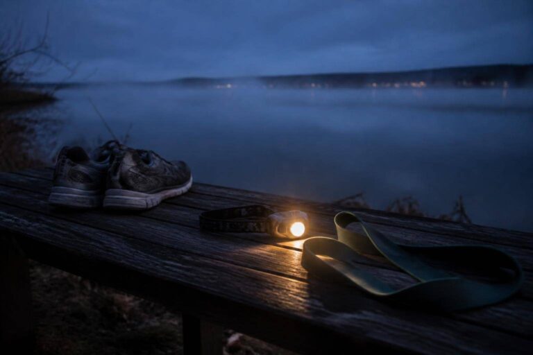 Stirnlampe, Laufschuhe und Widerstandsband auf einer Bank am nebligen Seeufer – Training im Winter am Bodensee